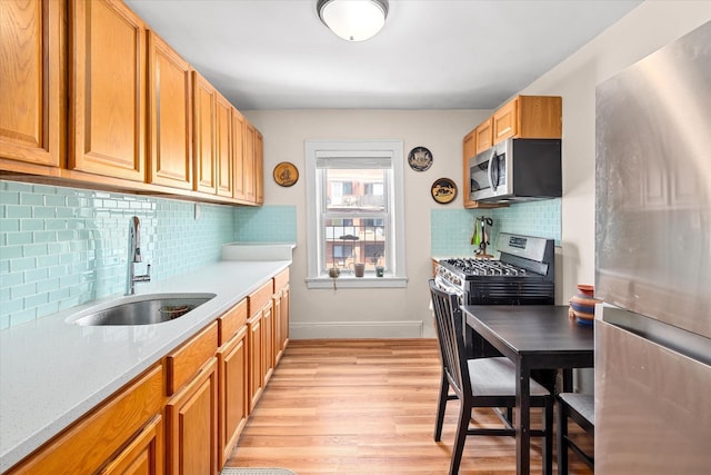 kitchen with light countertops, tasteful backsplash, light wood-type flooring, a sink, and appliances with stainless steel finishes