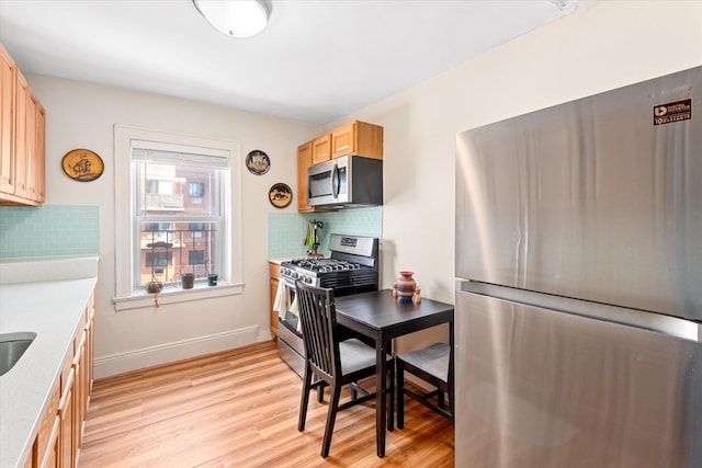 kitchen with light wood finished floors, baseboards, backsplash, and appliances with stainless steel finishes