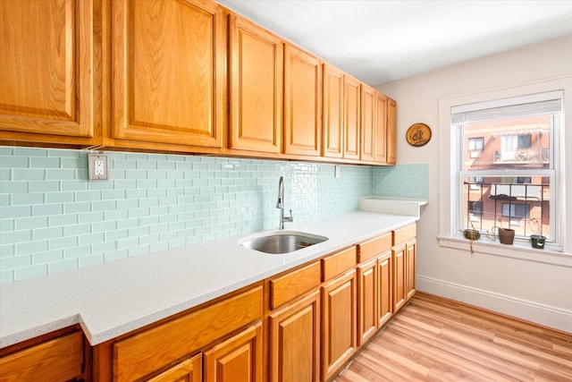 kitchen featuring light countertops, a sink, tasteful backsplash, and light wood-style flooring