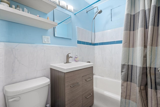 bathroom with tile walls, a wainscoted wall, toilet, vanity, and shower / bath combination with curtain