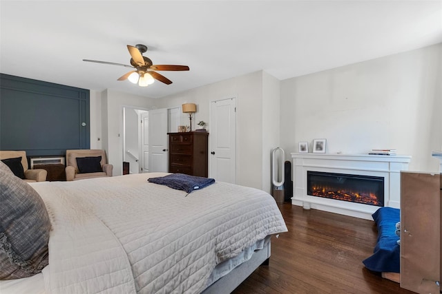 bedroom with a glass covered fireplace, wood finished floors, and ceiling fan