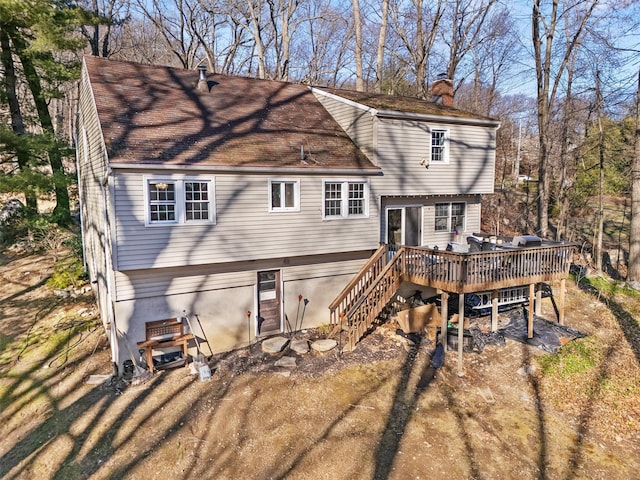 back of house featuring roof with shingles, a chimney, a deck, and stairway