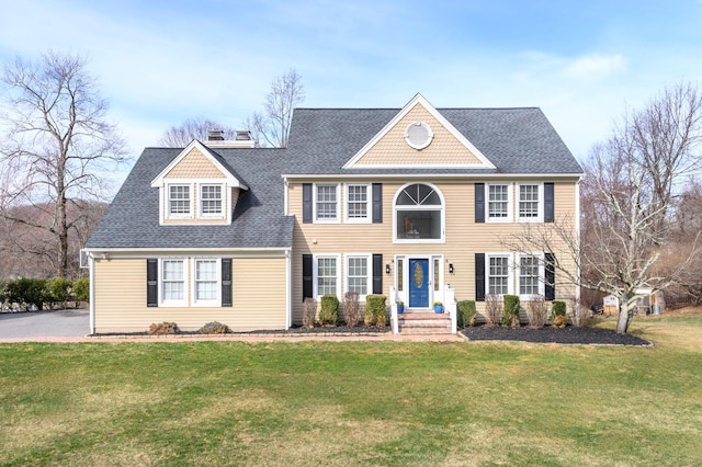 colonial home featuring a chimney, a shingled roof, and a front lawn