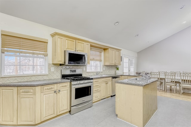 kitchen featuring vaulted ceiling, backsplash, light brown cabinetry, a peninsula, and appliances with stainless steel finishes