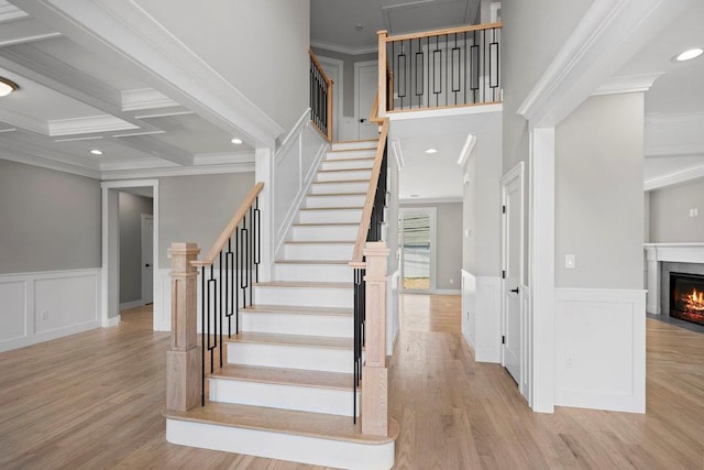407 Wellington Rd, East Meadow, NY 11554 - stairway featuring a fireplace with flush hearth, wood finished floors, beam ceiling, a wainscoted wall, and ornamental molding