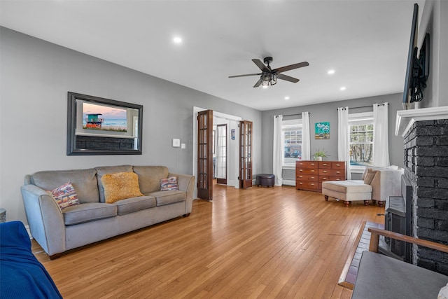 living area with a brick fireplace, ceiling fan, recessed lighting, baseboard heating, and light wood-style floors