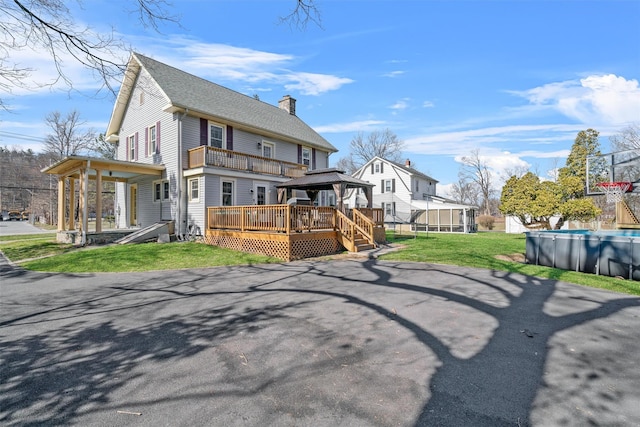 view of front facade with a front lawn, a chimney, a wooden deck, and a gazebo