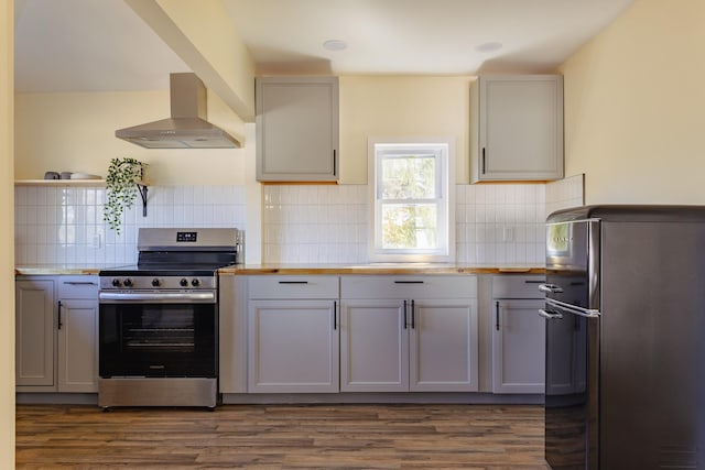 kitchen featuring dark wood-style flooring, gray cabinetry, stainless steel range with electric cooktop, freestanding refrigerator, and wall chimney exhaust hood