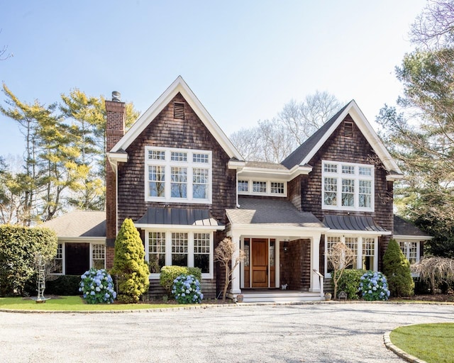 shingle-style home with a standing seam roof, a chimney, covered porch, and metal roof