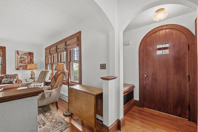 foyer entrance featuring light wood-style floors, baseboards, a baseboard heating unit, and arched walkways