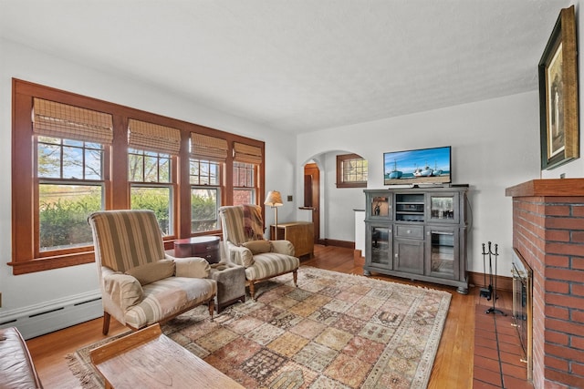living room with a baseboard heating unit, arched walkways, wood finished floors, and baseboards