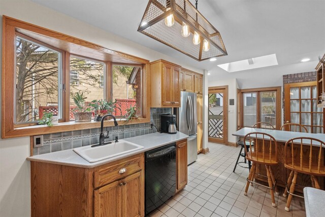 kitchen with a skylight, freestanding refrigerator, backsplash, dishwasher, and a sink