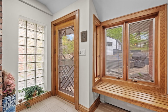 doorway with light tile patterned floors, vaulted ceiling, and baseboards