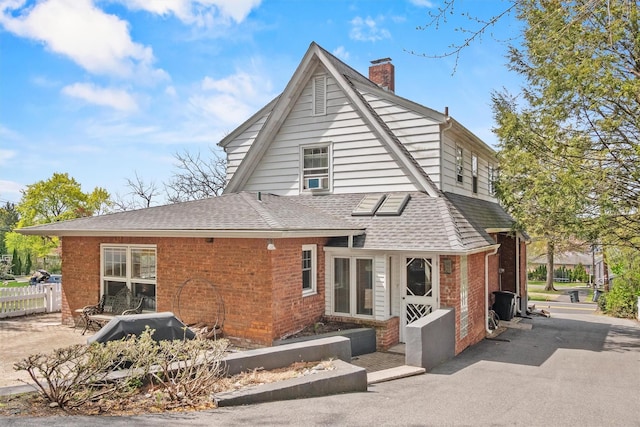 rear view of property featuring fence, a chimney, a shingled roof, and brick siding