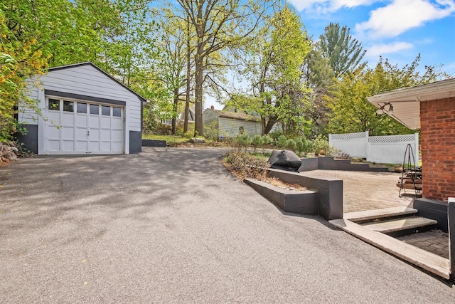 view of patio with fence, a detached garage, aphalt driveway, and an outbuilding