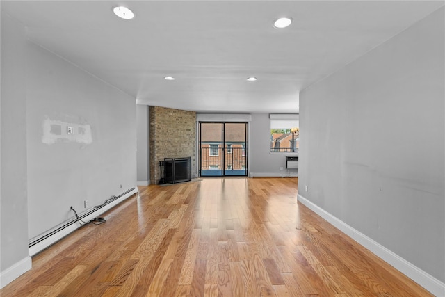 unfurnished living room featuring baseboards, baseboard heating, a brick fireplace, and light wood-type flooring