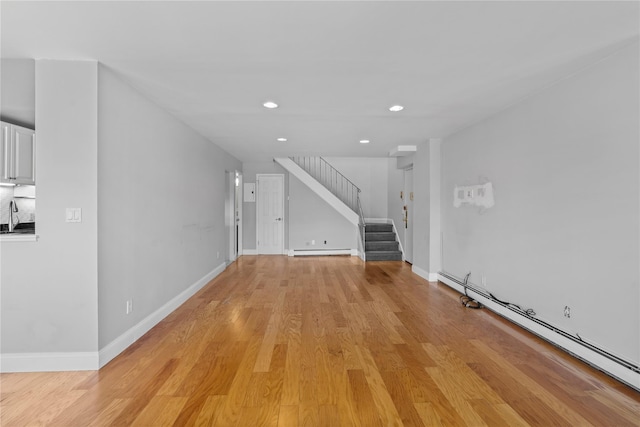 unfurnished living room with light wood-type flooring, baseboard heating, stairway, and a baseboard radiator