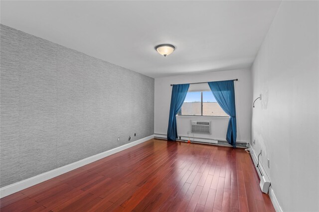 spare room featuring baseboards, an accent wall, a baseboard heating unit, and dark wood finished floors