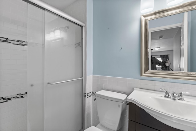 full bathroom featuring tile walls, wainscoting, a stall shower, vanity, and toilet