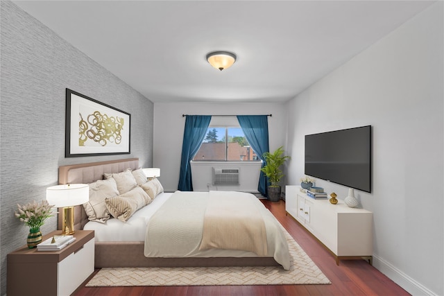 bedroom with an AC wall unit, an accent wall, baseboards, and wood finished floors