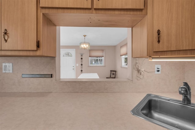 kitchen featuring a notable chandelier, backsplash, light countertops, and a sink