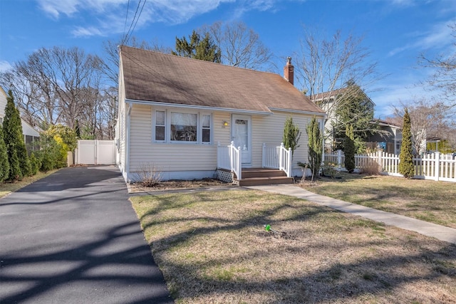 view of front of home featuring a front lawn, aphalt driveway, fence, roof with shingles, and a chimney