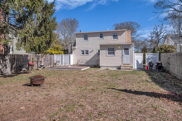 rear view of property featuring a gate, a fenced backyard, a lawn, and an outdoor fire pit