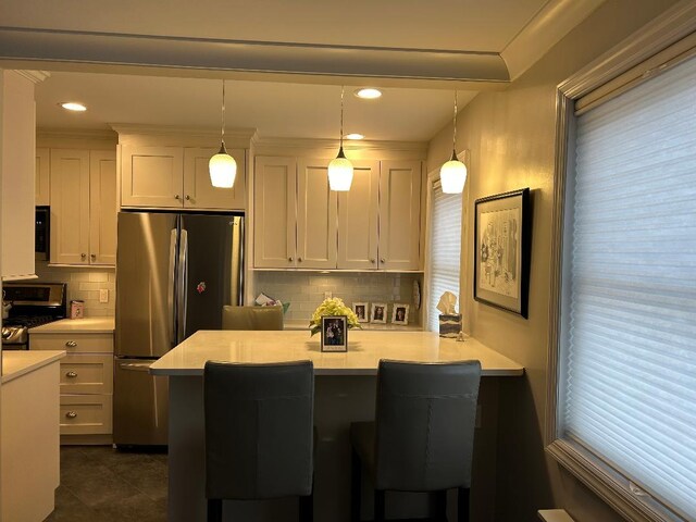 kitchen with light countertops, pendant lighting, white cabinetry, a kitchen breakfast bar, and stainless steel appliances
