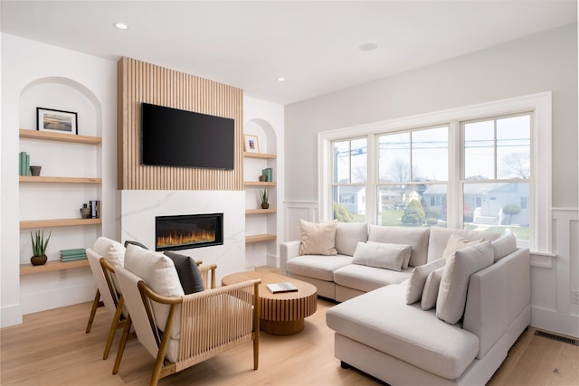 living room with wood finished floors, wainscoting, a high end fireplace, built in shelves, and visible vents