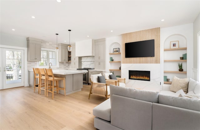 living area with recessed lighting, a premium fireplace, light wood-style flooring, and built in shelves
