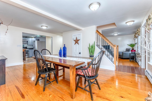 dining space with stairs, baseboards, light wood finished floors, and a baseboard radiator