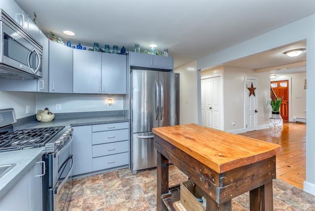 kitchen with a baseboard heating unit, stone finish flooring, dark countertops, stainless steel appliances, and baseboards