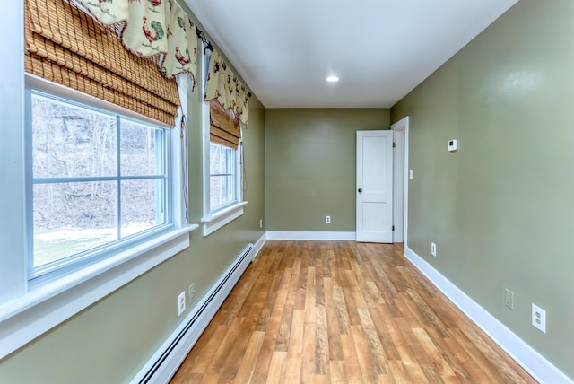 unfurnished room with a baseboard heating unit, baseboards, and light wood-style floors