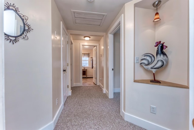 hallway with baseboards, visible vents, and light carpet