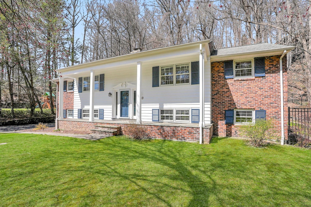 raised ranch featuring covered porch, a front yard, and brick siding
