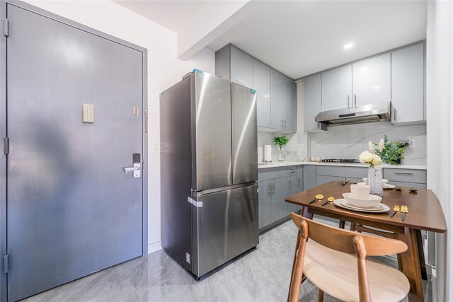 941 57th St Unit 4B, Brooklyn, NY 11219 - kitchen with gray cabinetry, under cabinet range hood, tasteful backsplash, freestanding refrigerator, and light countertops
