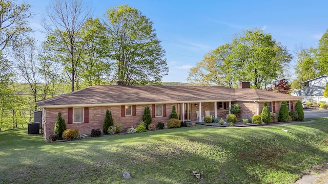 ranch-style home with a front lawn, a chimney, brick siding, a porch, and central air condition unit