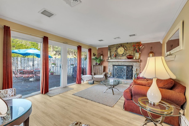 living room featuring visible vents, crown molding, wood finished floors, and a stone fireplace