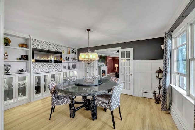 dining area with crown molding, a decorative wall, baseboard heating, a baseboard heating unit, and light wood finished floors