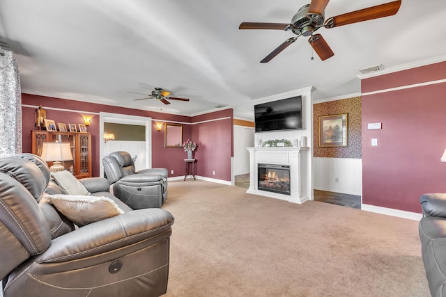 carpeted living room featuring a ceiling fan, visible vents, baseboards, a glass covered fireplace, and ornamental molding
