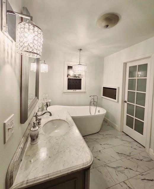 full bathroom featuring vanity, marble finish floor, baseboards, a chandelier, and a soaking tub