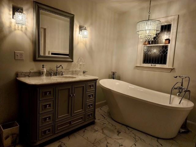 full bathroom featuring a freestanding bath, vanity, baseboards, marble finish floor, and a notable chandelier