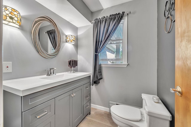 half bath featuring toilet, baseboards, wood finished floors, and vanity