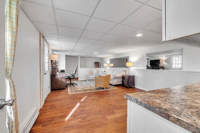 living area with a baseboard heating unit, recessed lighting, wood finished floors, and a paneled ceiling