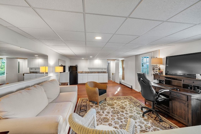 living room with plenty of natural light, a baseboard heating unit, a drop ceiling, and wood finished floors