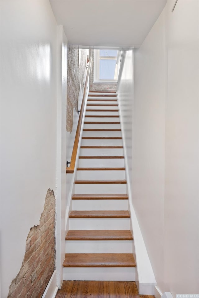 stairs with brick wall and wood finished floors