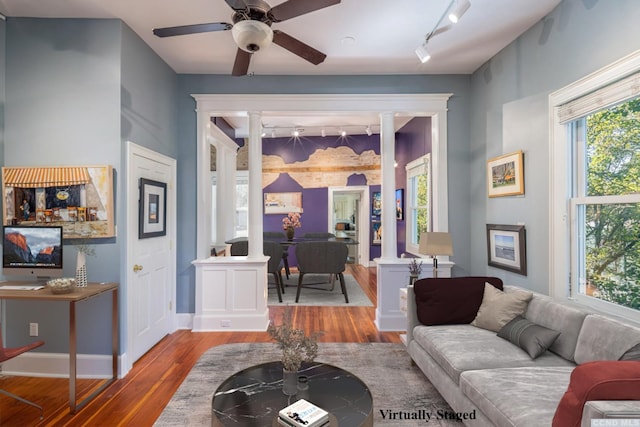 living area featuring wood finished floors, ceiling fan, baseboards, track lighting, and ornate columns