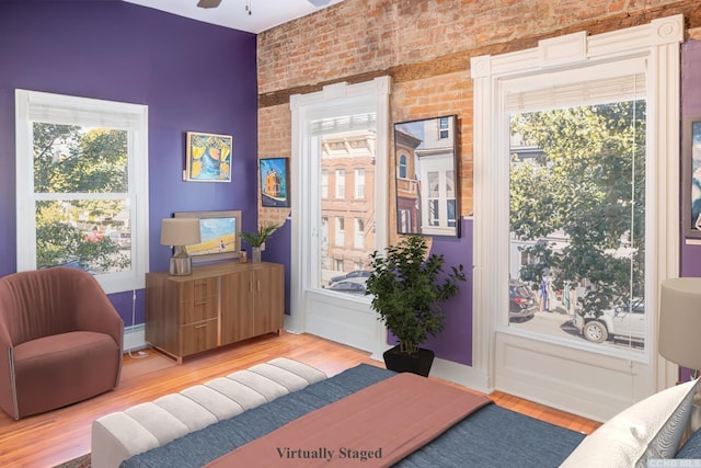 living area featuring light wood-style flooring, brick wall, and ceiling fan
