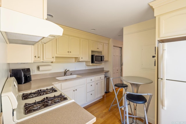 kitchen featuring a sink, freestanding refrigerator, gas range oven, stainless steel microwave, and extractor fan