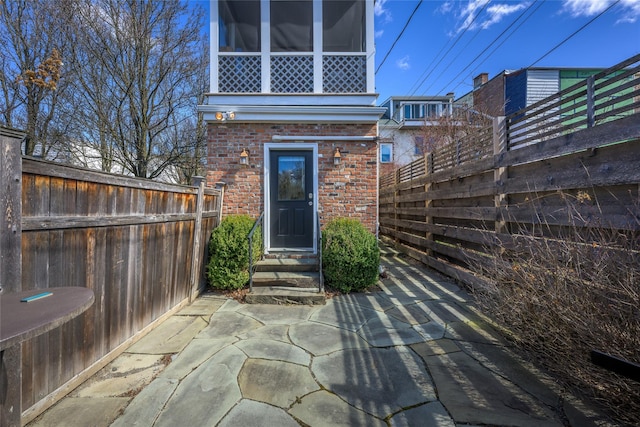 view of exterior entry featuring a patio, brick siding, and fence